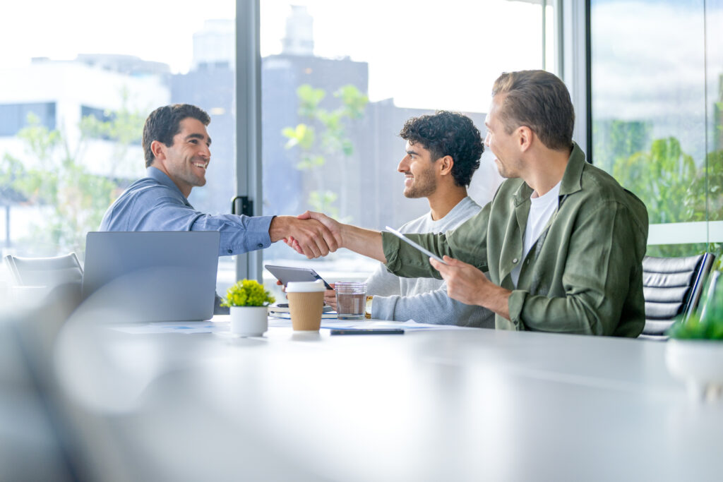 A mortgage broker shaking hands with businessmen in a brightly lit, professional office environment to celebrate a successful loan approval.